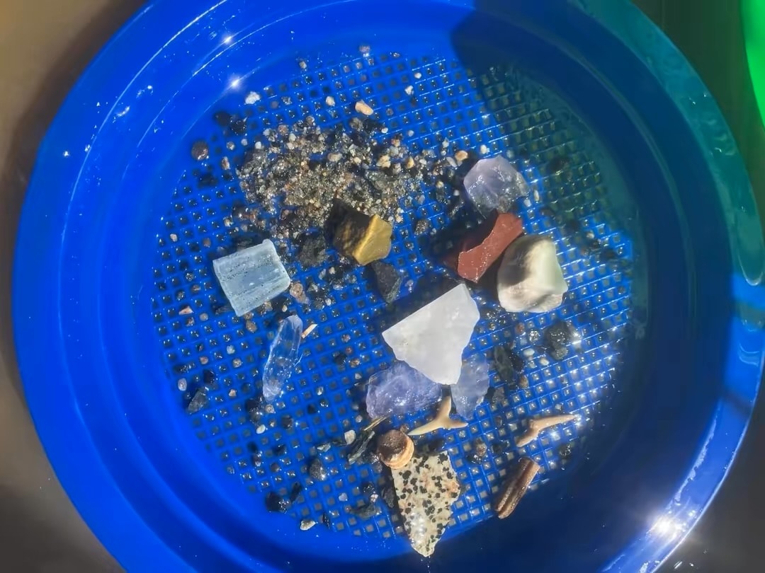 Colorful gemstones and fossils in a blue sieve
